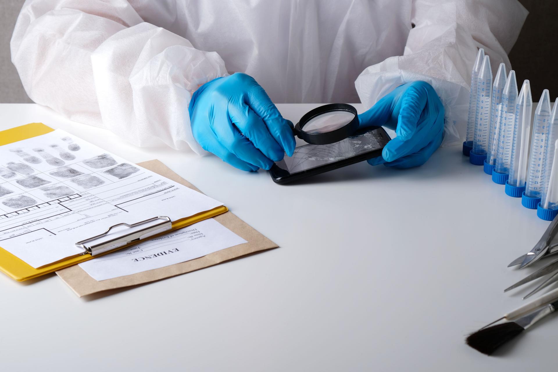 A forensic forensic expert examines a broken phone with a magnifying glass, analyzes evidence from the crime scene